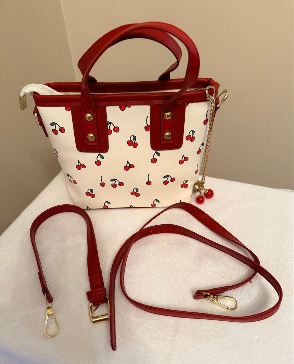White faux-leather tote bag features a vibrant red cherry pattern.